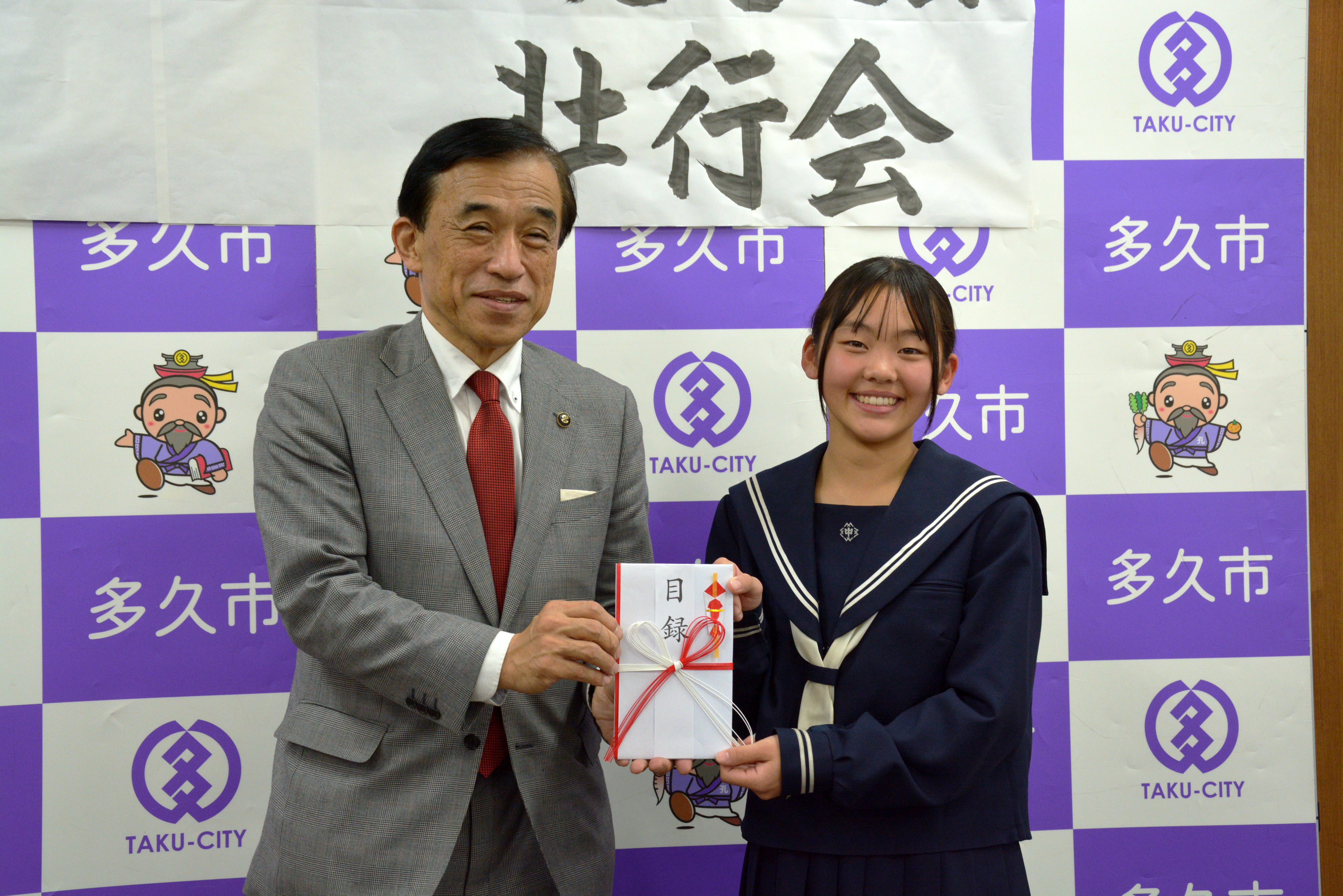 横尾市長から緒方主将へ目録が手渡されました