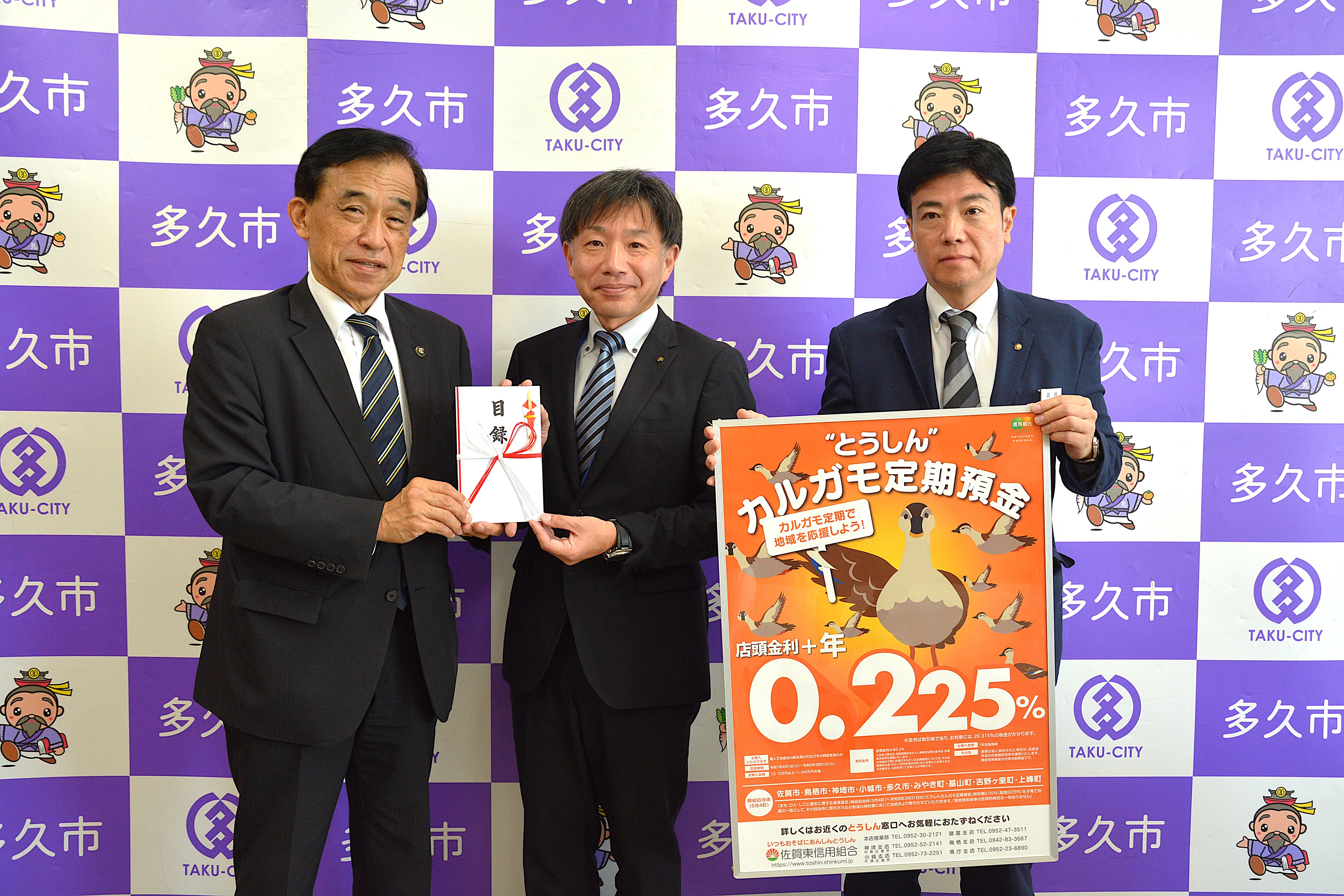 目録を手にする柿本営業支援部長（中央）と横尾市長（左）、チラシを掲げる小城支店徳島智史支店長（右）
