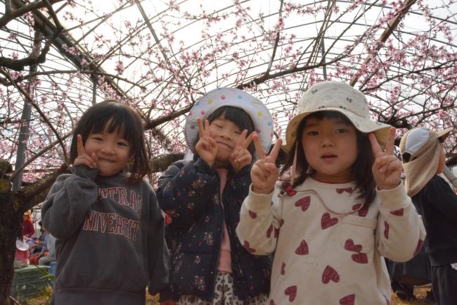 桃の花をバックにポーズをとる子どもたち