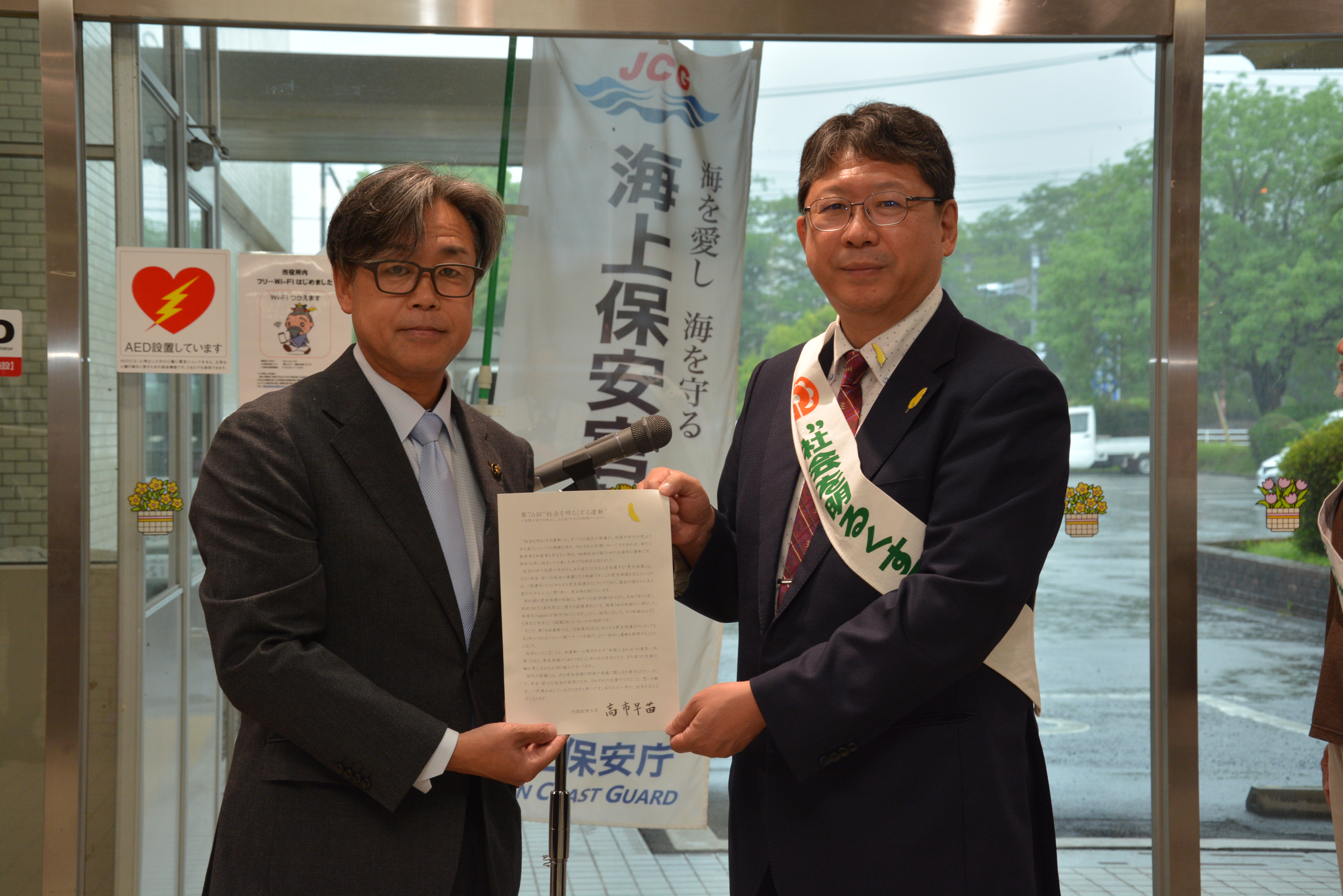 社会を明るくする運動　写真（香月正則市長と佐賀保護観察所久保山企画調整課長が伝達メッセージを持ち合っているようす）
